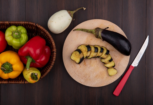 top view colored bell peppers with cucumbers and tomatoes in a basket with eggplants on a cutting board with a knife on a wooden background - Гречневая каша с баклажаном
