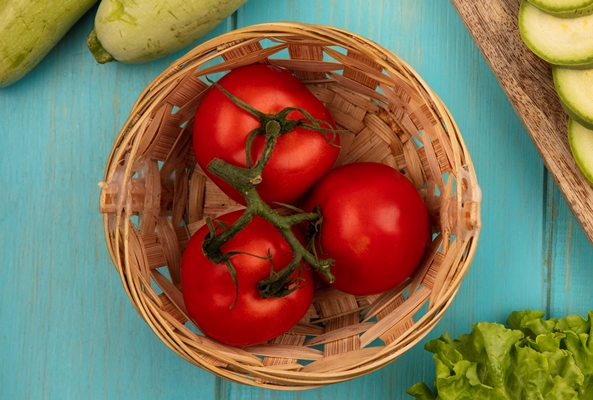top view of fresh tomatoes on a bucket with chopped zucchinis on a wooden kitchen board with celery with lettuce isolated on a blue wooden surface - Рагу из красного перца с кальмаром