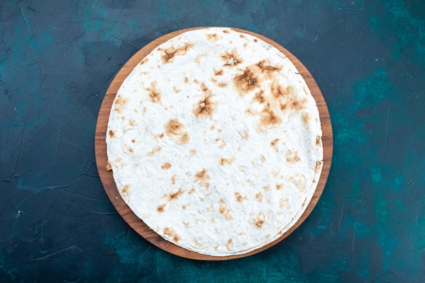 top view of round plain pita baked bread like dough on dark blue surface - Бутерброды с паштетом из белой фасоли