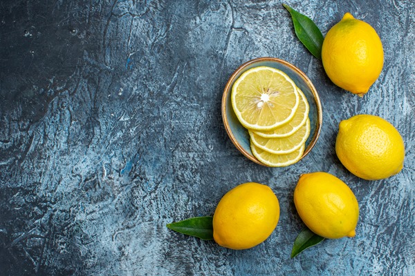 top view of whole and cut fresh lemons with leaves on the left side on dark background - Цитрусовый чай с имбирём и карамболой