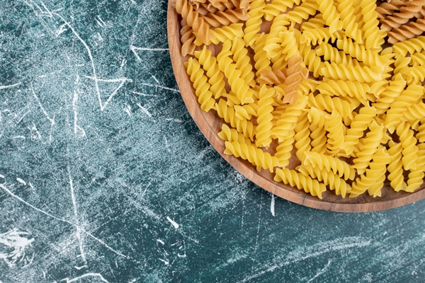 yellow raw fusilli pasta on wooden plate - Постные макароны с креветками и чесноком
