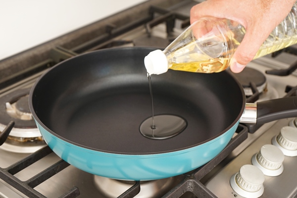 a man pours oil from a bottle into a frying pan in the kitchen home cooking - Яичница-болтунья