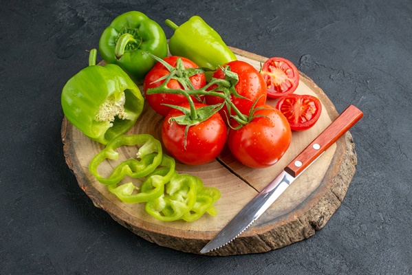 close up view of whole cut chopped green peppers and fresh tomatoes knife on wooden cutting board on black surface - Фриттата с картофелем