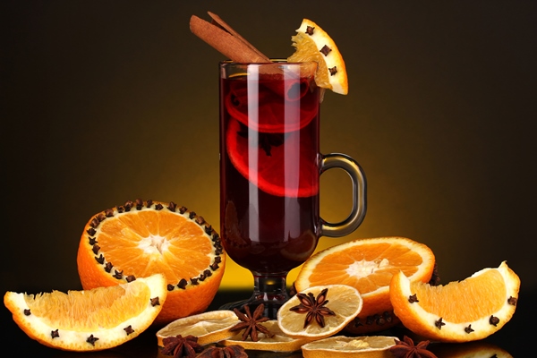 fragrant mulled wine in glass with spices and oranges around on yellow background - Безалкогольный глинтвейн на смеси соков