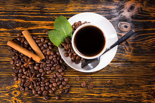 freshly brewed cup of espresso coffee with roasted whole coffee beans mint star anise and stick cinnamon spices on a rustic wooden table overhead view - Кофейный сбитень