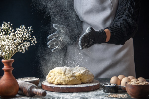 front view female cook rolling out dough with flour on dark job raw dough bakery pie oven pastry hotcake - Баурсаки