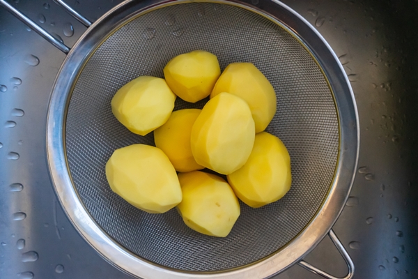 high angle shot of raw peeled potatoes in a strainer in the kitchen sink - Суп картофельный с крупой и мясом