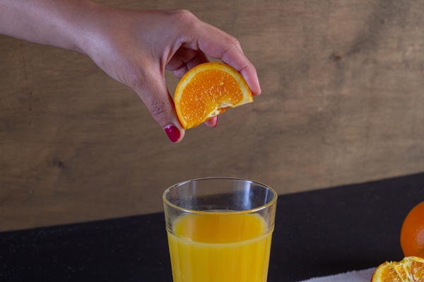 mano de una mujer exprime el zumo de naranja en un vaso sobre una mesa fondo de fruta de naranja - Безалкогольный яблочный глинтвейн с апельсином