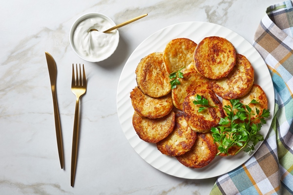 potato pancakes with cottage cheese with garlic parsley served with sour cream dip on a plate on a light marble stone background with golden cutlery top view close up - Драники с луком, сыром и чесноком