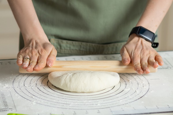 rolling out the dough with a wooden rolling pin on a silicone baking mat view of hands and workspace - Баурсаки