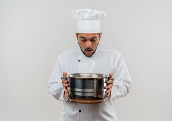 surprised young male cook in chef uniform holding and looking inside pot isolated on white space - Правила приготовления заправочных супов
