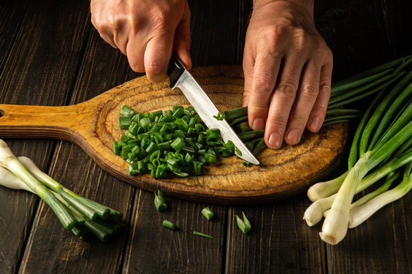 the chef cuts green onion leaves on a vintage cutting board before preparing a delicious dish - Макароны с яйцом