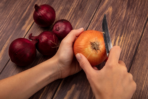 top view of female hands cutting a yellow onion with knife with red onions isolated on a wooden wall - Котлеты, фаршированные яйцом