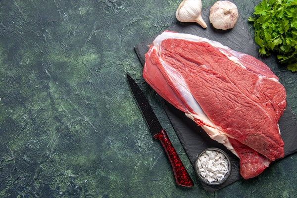 top view of raw fresh red meat and salt green bundle knife on cutting board on the left side on green black mix colors background - Бульон с мясными фрикадельками