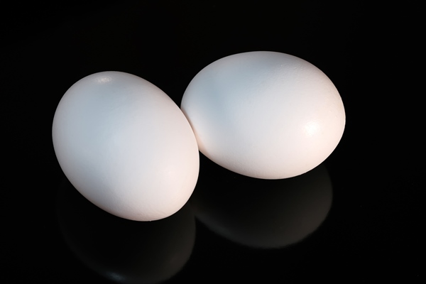 two white raw chicken eggs lie on a black reflective table close up - Стручковая фасоль с яйцом