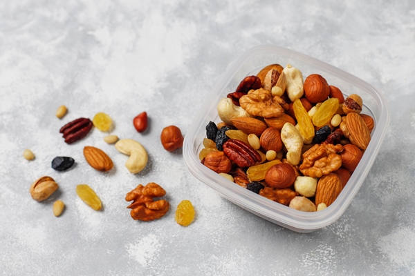 assortment of nuts in plastic container cashew hazelnuts walnuts pistachio pecans pine nuts peanut raisins top view - Гурьевская каша