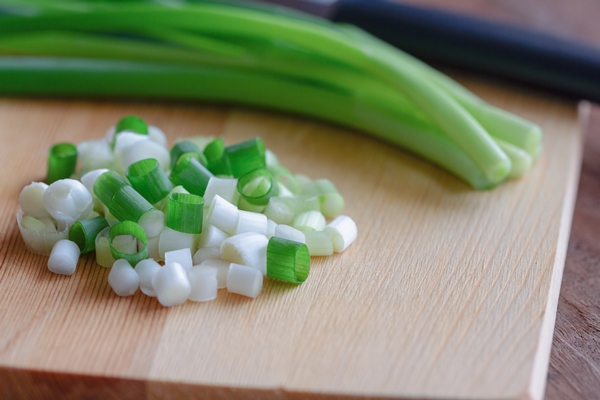 close up view on chopped fresh spring onion and knife put on wood cutting board - Картофельный салат с огурцами и яйцом