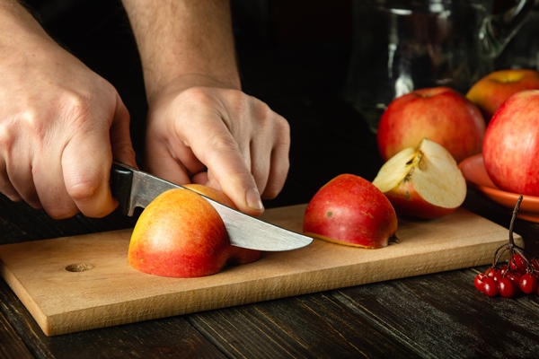 closeup of a chef hands with a knife slicing apples on a cutting wooden board for making delicious fruit drink the idea of the apple diet copy space - Салат с огурцом, морковью и яблоком