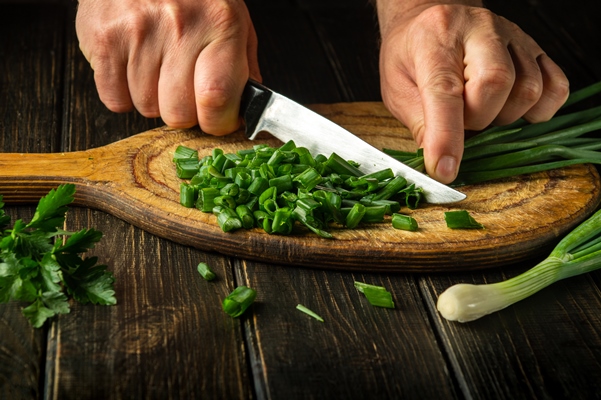 cook cutting green onion on a cutting board with a knife for preparing vegetarian dish peasant food - Салат из сельди