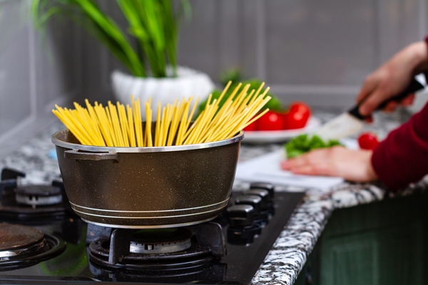 cooking spaghetti in a saucepan in a kitchen at home - Спагетти в сливочном соусе с ветчиной