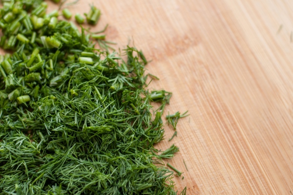 finely chopped fresh dill on a wooden cutting board with blurred edges - Салат "Оливье"