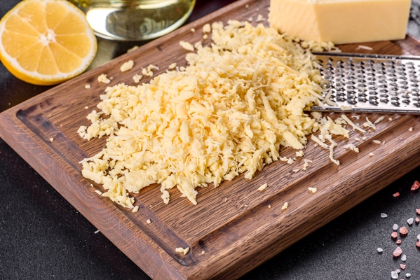 fresh hard cheese grated on a large grater on a wooden cutting board on a dark concrete background - Куриный суп с кукурузой и сыром