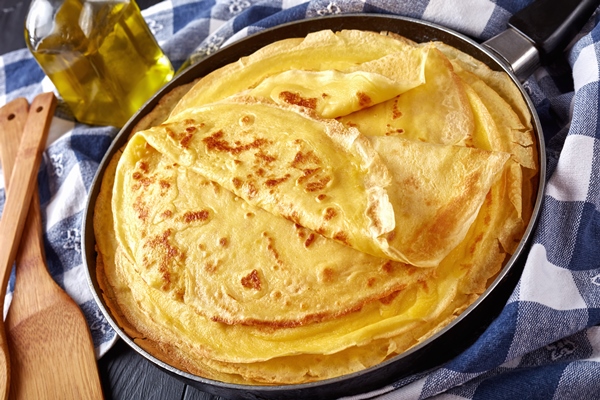 freshly fried homemade french crepes on a skillet on black wooden table with kitchen towel - Блинчики с творогом, изюмом и сметаной