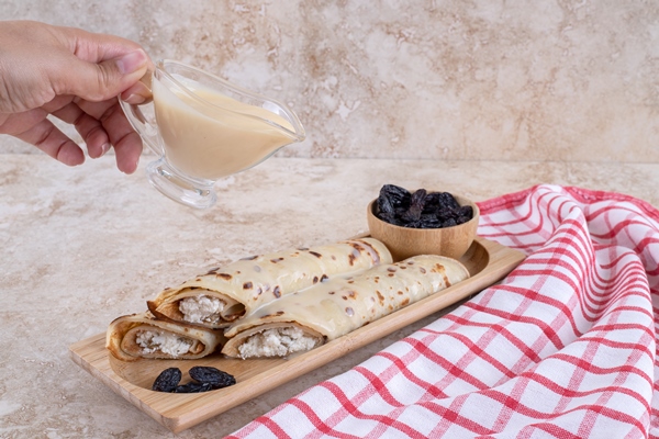 hand pouring condensed milk on homemade crepes high quality photo - Блинчики с творогом, изюмом и сметаной