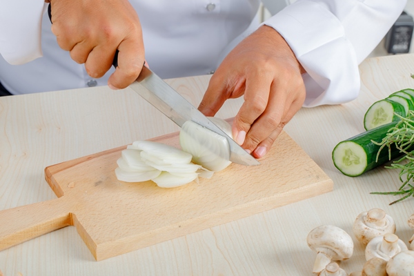 male chef chopping onion on cutting board in kitchen in uniform - Сливочный суп с грибами и булгуром