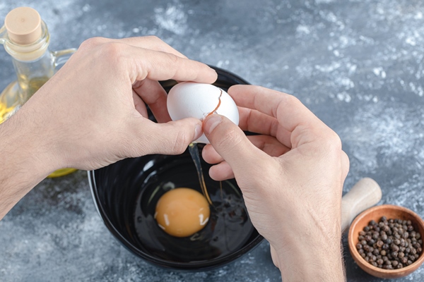 man hands breaking eggs in bowl over grey table - Лапшевник с мясом