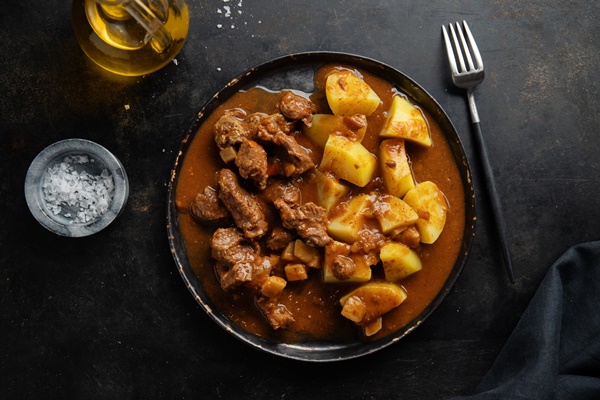 meat with potato stew served on plate on dark background - Мясной гуляш