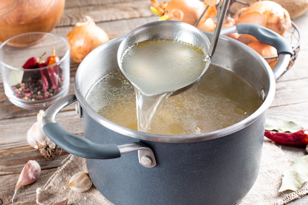 saucepan with bouillon with a ladle on the table bone broth - Язык отварной под соусом