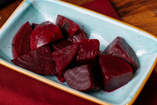 side view of slices of cooked beet in a plate on a wooden table - Винегрет с консервированным мясом