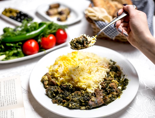 side view woman eating traditional azerbaijani dish shabzi pilaf fried meat with greens boiled rice with vegetables herbs - Выбор гарниров и соусов к мясу