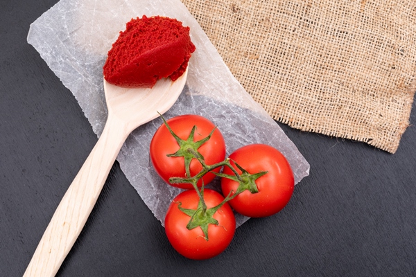 tomatoes on polyethylene tomato paste in wooden spoon near the sackcloth on black stone surface - Солянка по-грузински