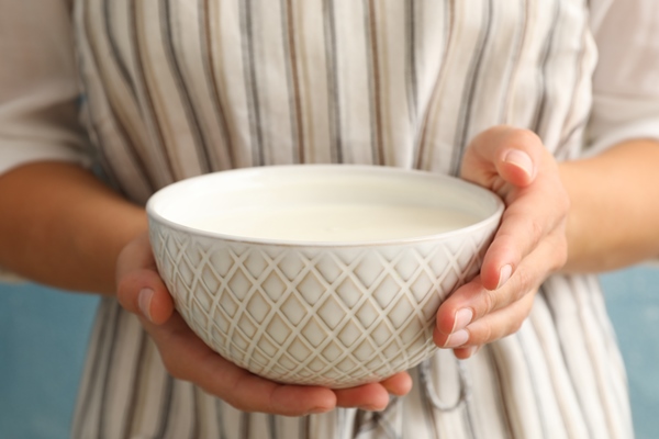 woman in apron hold bowl of sour cream yogurt against blue - Томатный суп-пюре с молочным соусом