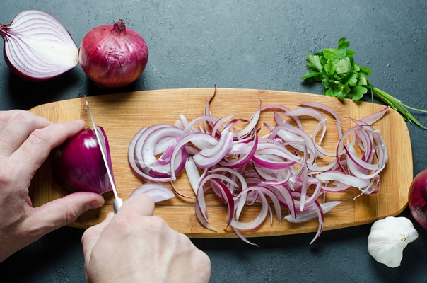a man cuts red onions on a wooden chopping board with a kitchen knife preparing food hands close up - Бефстроганов