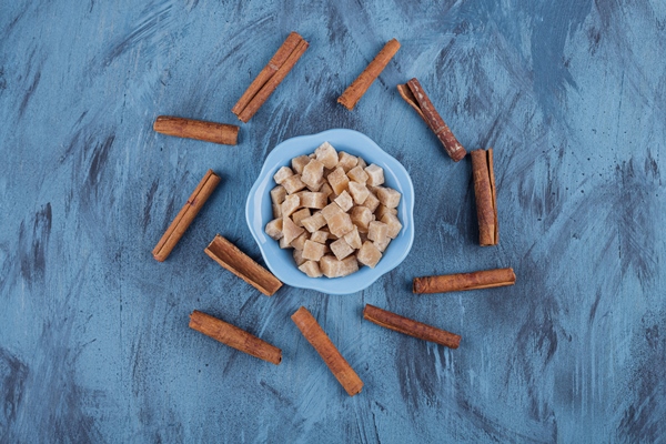 blue bowl of brown sugar cubes and cinnamon sticks on blue surface - Панкейки с корицей