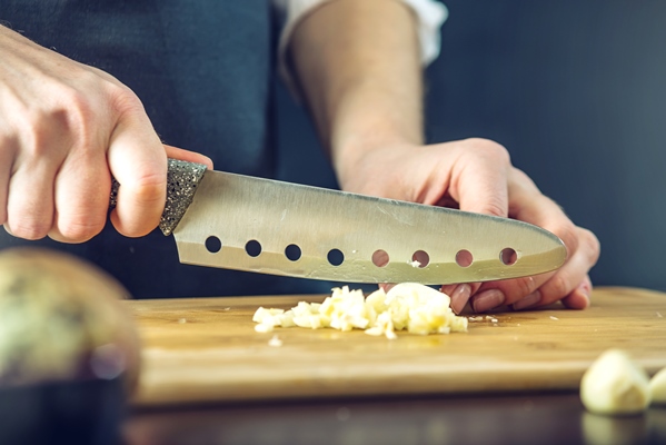 chef in black apron cutting garlic with a knife - Шампиньоны в горчичном маринаде