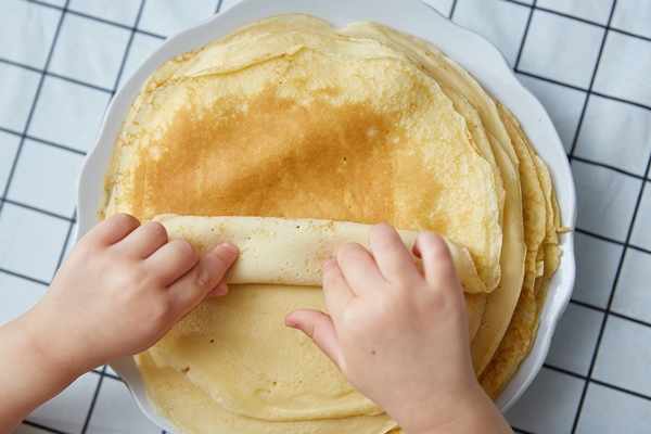 children s hands take a pancake from a stack top view - Блинчики с рыбой и рисом