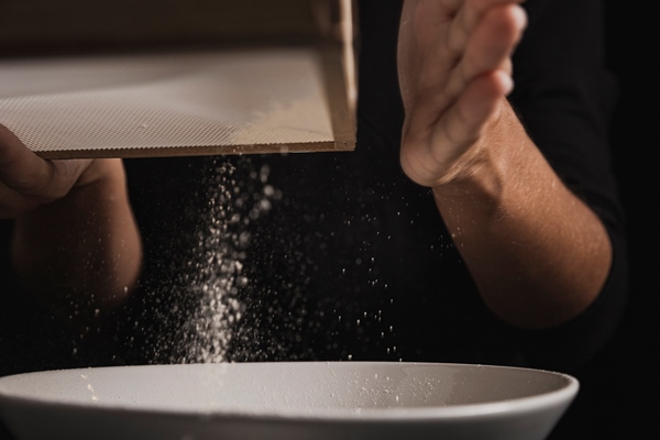 close up view hand sifting flour - Дрожжевое сдобное тесто