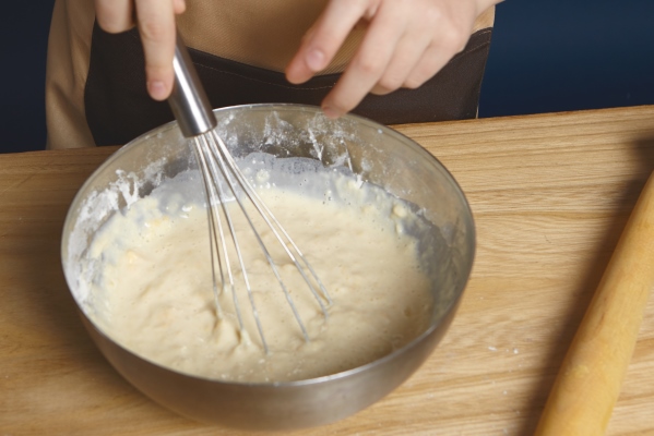 cropped shot of hands holding beater while beating eggs with flour for pine cakes in metal bowl - Монастырская кухня: тыковник с черносливом и постные оладьи