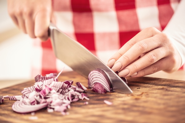 detail of female hands cutting a red onion on a chopping board - Монастырская кухня: чечевичный суп, хлопья в яблоках