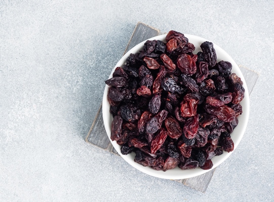 dried raisins from dark grapes in a plate on a gray concrete - Монастырская кухня: овсяная каша, закуска из баклажанов