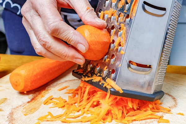 female hand grating fresh bright orange carrot on stainless steel grater - Монастырская кухня: рисовые тефтели с ржаными хлебцами