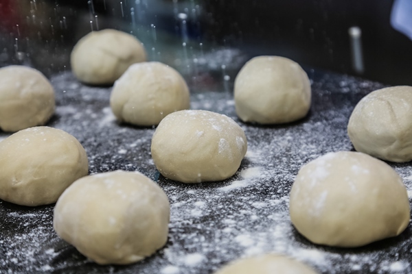 flour pouring on formed dough bolls on black board side view - Сдобные ватрушки
