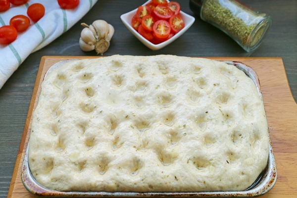 focaccia bread dough sprinkled with olive oil after marking dimples with fingertips - Фокачча с помидорами и луком