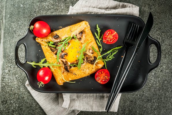 french cuisine breakfast lunch snacks vegan food traditional dish galette sarrasin crepes with eggs cheese fried mushrooms arugula leaves and tomatoes on black stone table - Ленивые хачапури