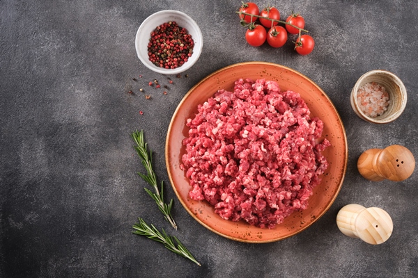 fresh raw mince minced beef ground meat with herbs and spices in plate top view - Беляши