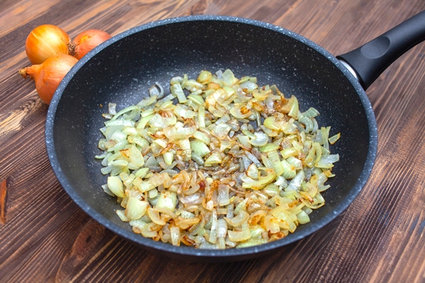fried onions in a pan top view brown wooden background three bulbs - Запеканка с мясом